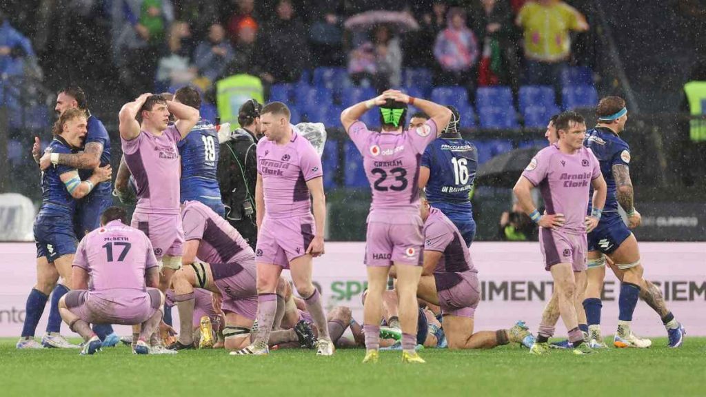 Scotland's dejected players look on in disbelief as Italy celebrate a famous win in the Roman rain